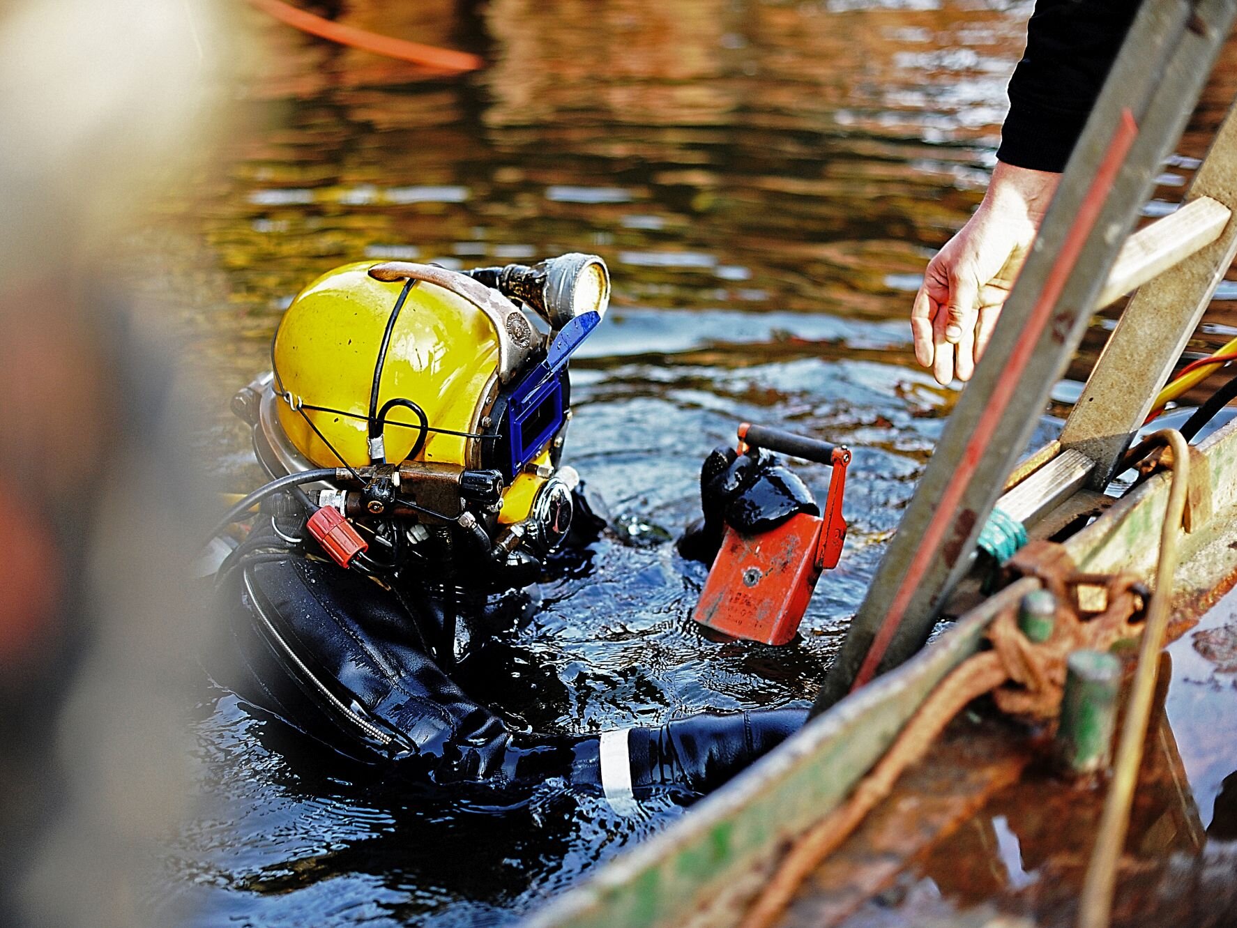 Taucher mit gelbem Helm und schwarzem Anzug steigt an einer Leiter aus dem Wasser.