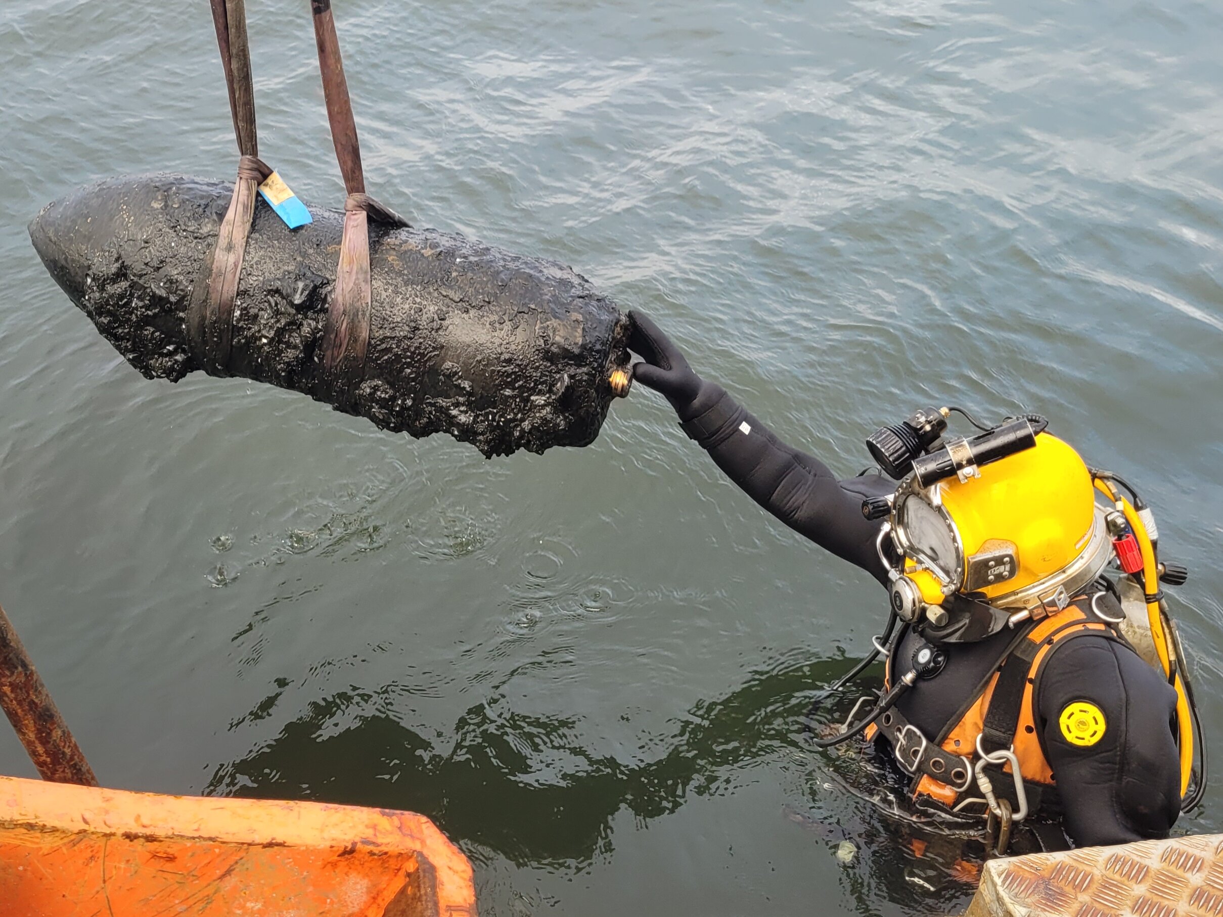 Diver in sea water with muddy UXO hanging on a rope